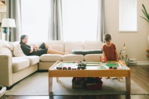 Mother holding newborn sits on couch watching other child play