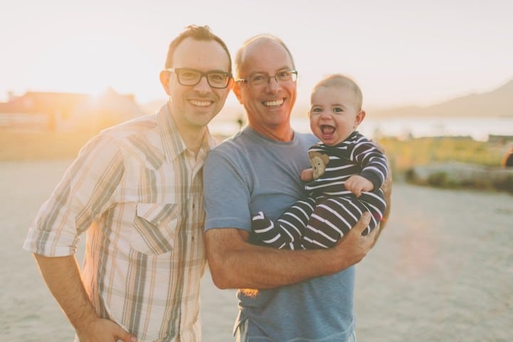 Father, grandfather, and baby have fun on the beach at sunset
