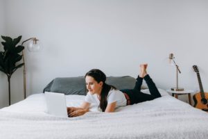 Young woman working on laptop while lying on her bed