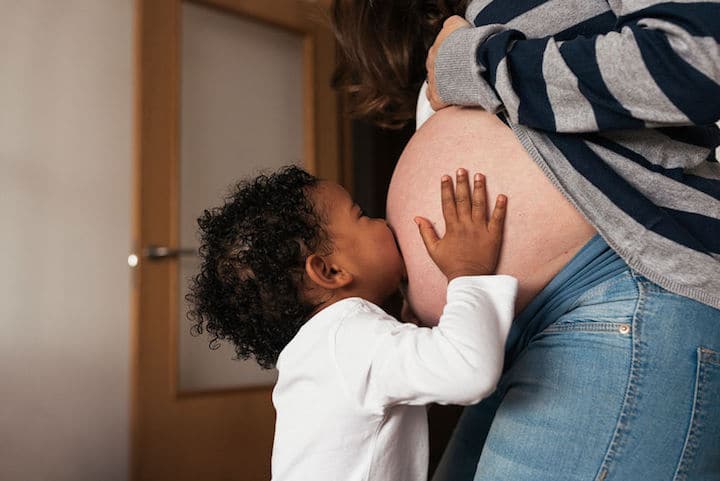 beautiful multi-racial girl kisses her pregnant mother's belly