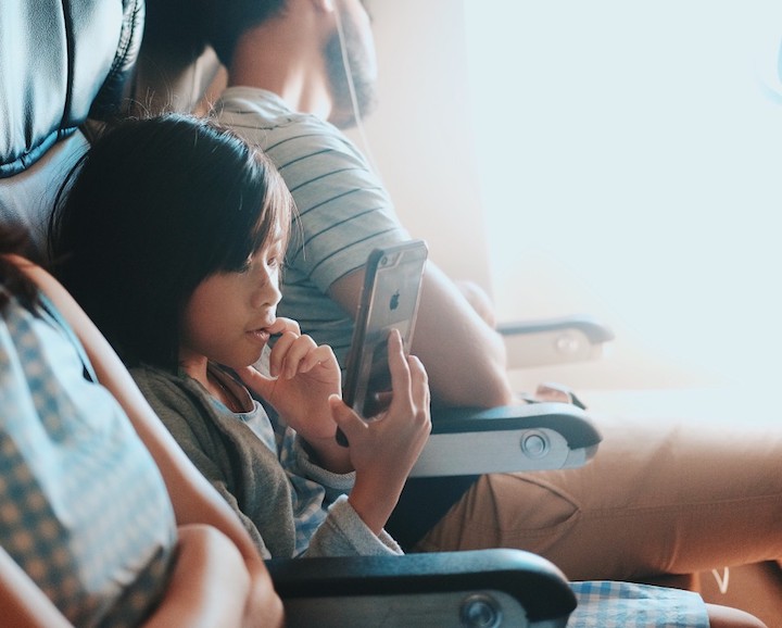 Child sits between parents on airplane, playing on smartphone