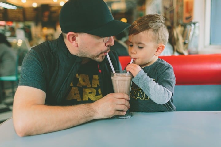 A dad and his son split a milkshake with two straws