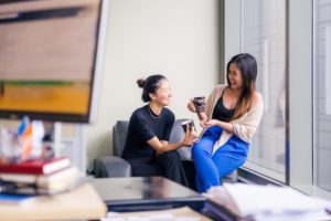 Two young ladies laugh over a cup of coffee in the office