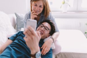Husband and wife looking at phone together and cuddling on couch