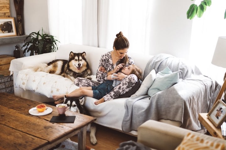 Mom cuddles on couch with two dogs and kid
