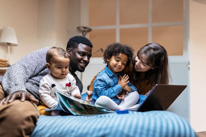 Family sits on bed, parents reading toddlers books