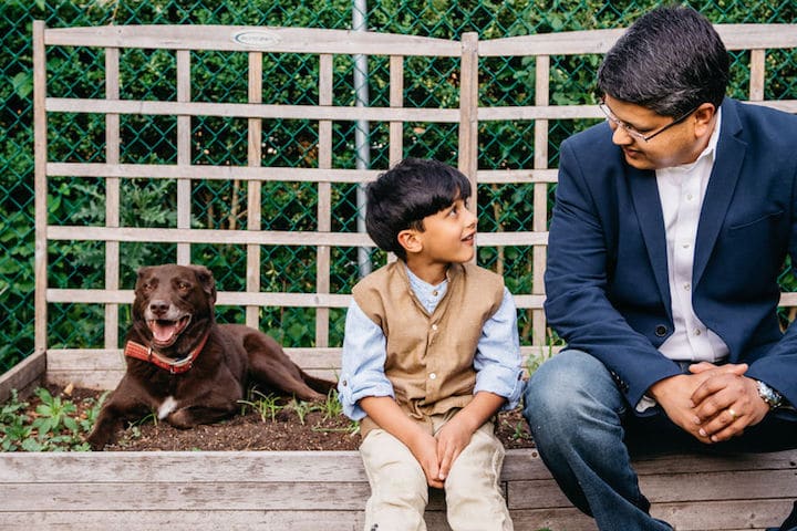 A dad has a nice conversation with his son as they sit in the garden with their dog