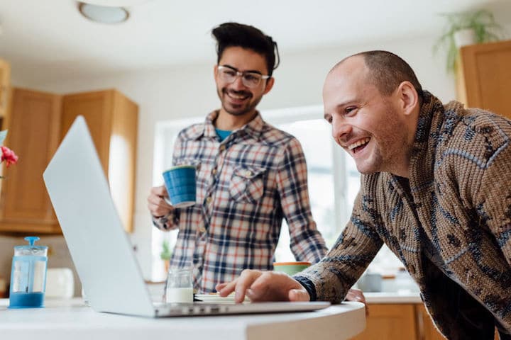 A male gay couple drinks coffee and surfs the web in their kitchen