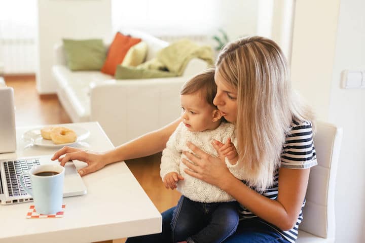 A young mother balances her baby on her lap while she tries to get some work done on her computer