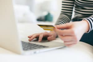 Closeup of a young woman's hands as she uses her credit card and laptop to pay for a purchase online