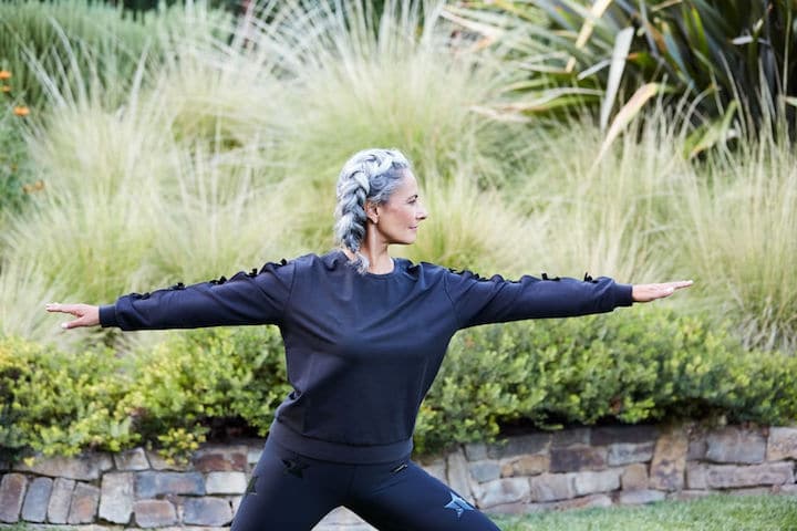 An older woman with a beautiful grey braid does yoga in her expansive backyard