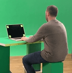 Man sitting in front of computer and green screen.