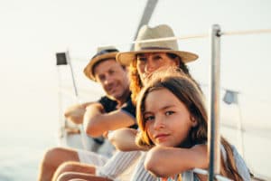A husband, wife, and their teenage daughter lean over the side of a boat on a sunny day