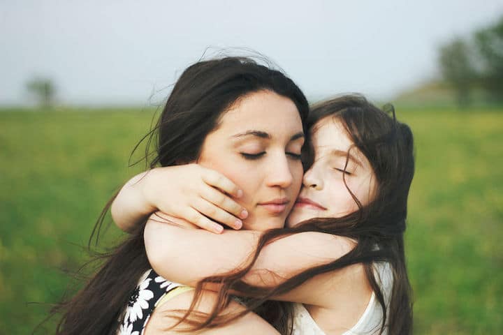Two sisters hug tightly outdoors in the wind