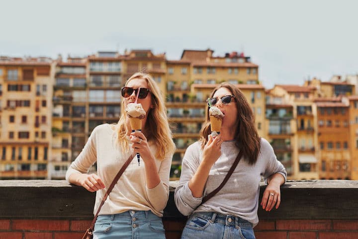 Two beautiful friends stand side by side as tourists in Italy, eating ice cream