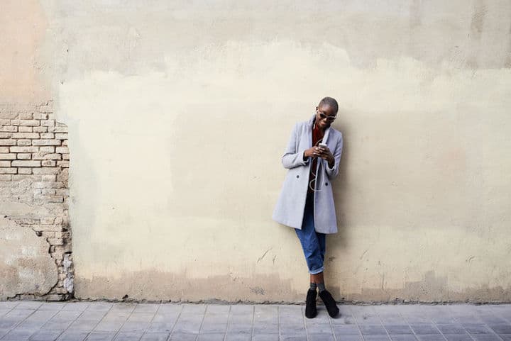 Stylish woman checks her phone in front of a rustic wall