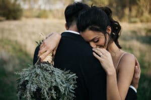 A young bride smiles, leaning into her groom's shoulder with her bouquet in her hands