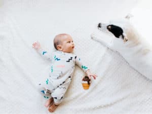 baby laying with dog on a white bed