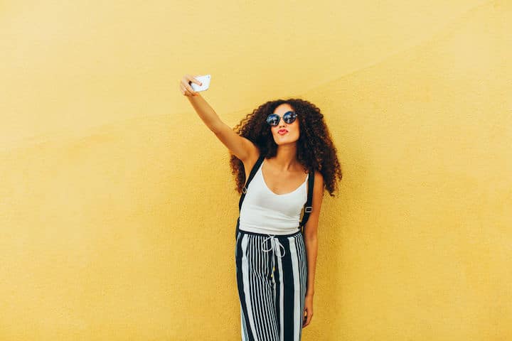 Chic young woman takes a selfie in front of a yellow wall