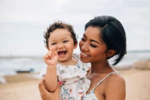 Mother holds her laughing baby on the beach