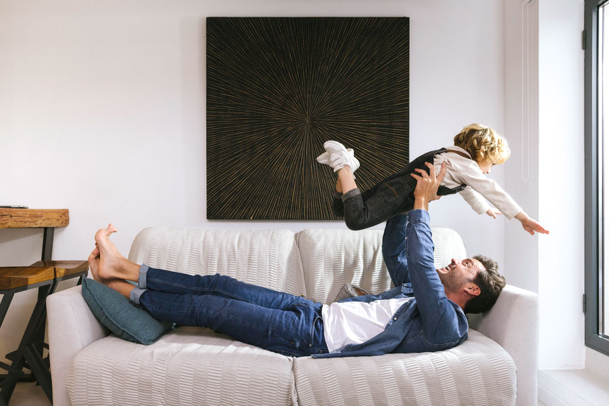 Dad laying on the couch while carrying child up in the air. Both are smiling