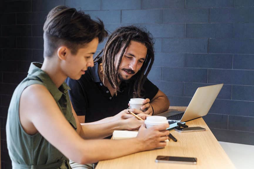 Eccentric man with dread locks and women with short hair work on a computer while drinking coffee in an office setting