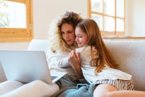 happy attractive young adult woman sitting on couch with her daughter with laptop on lap, smiling