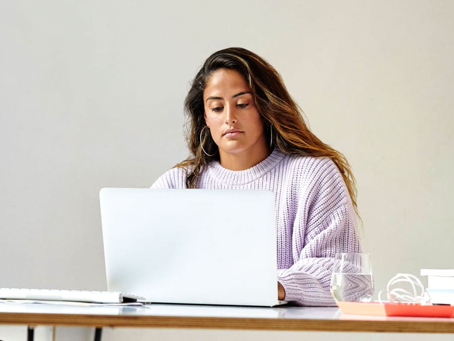 A girl sitting at a computer desk looking at a laptop
