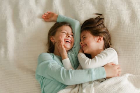 Sisters lying in bed laughing and embracing