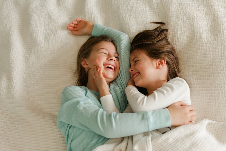 Sisters laying in bed laughing and embracing