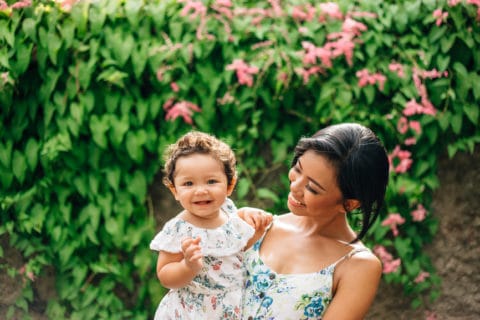 woman standing outside holding a smiling girl in beautiful floral sundresses.