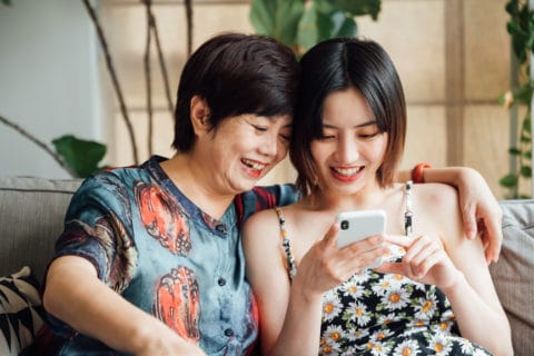 Adult child and mother looking at her phone on the sofa and smiling