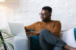 Afro-American entrepreneur sitting on a couch in his living room working on his laptop