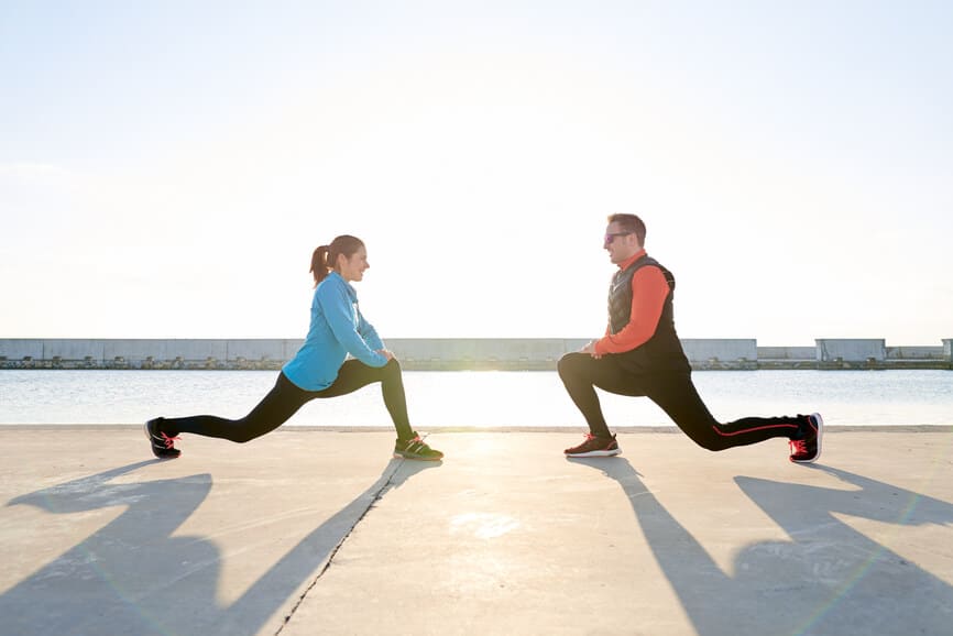 Side view of sportive couple stretching on pier in sunlight