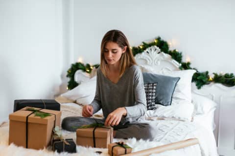 Woman sitting on bed wrapping presents