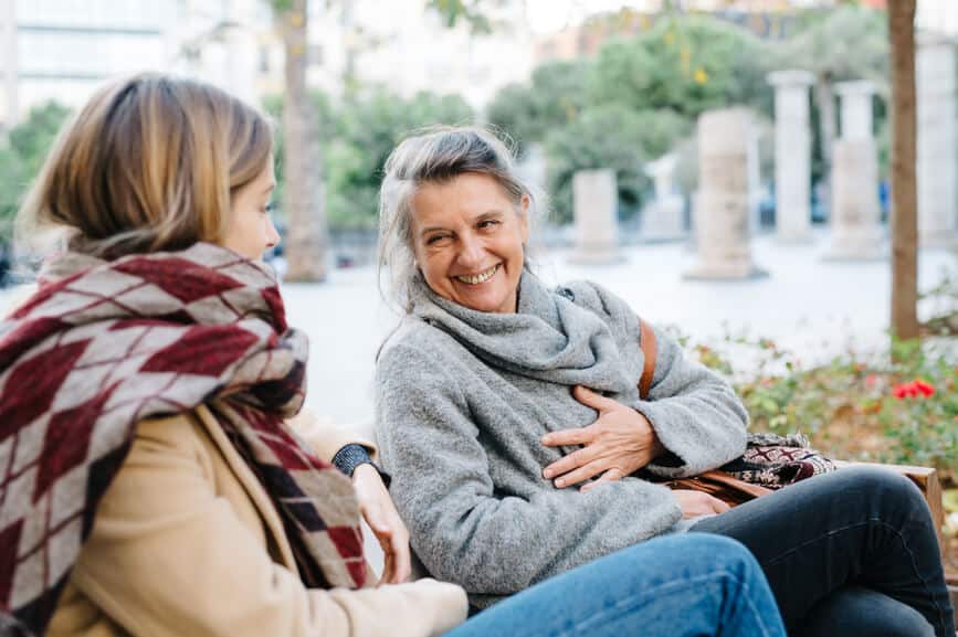 Elderly woman sitting in garden near her young daughter and laughing at good joke.