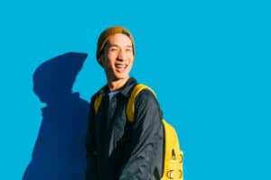 Portrait of happy stylish young asian man posing in front of a blue wall and looking at camera