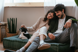 Smiling loving couple relaxing on sofa and caressing small Chihuahua dog while spending time together at home