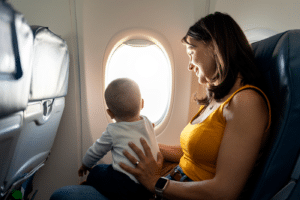Proud mother caring her son on airplane. The unrecognizable baby is looking through window