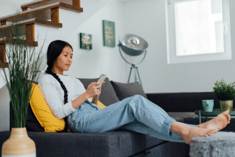 Woman sitting on sofa while browsing on internet on the phone