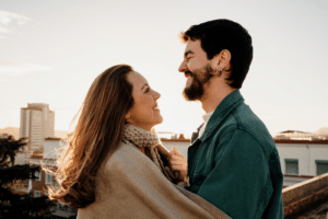 Portrait Of Cute Couple Looking At Each Other And Hugging On Rooftop During Sunset
