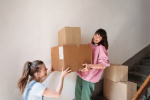 Two beautiful young women carrying boxes together, walking up stairs, moving in