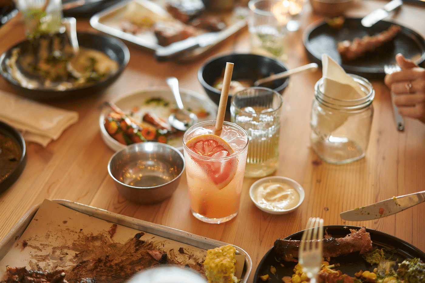 A pink grapefruit mocktail on a busy dinner table surrounded by plates of bbq food being eaten
