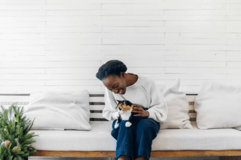 Attractive young black woman sitting on sofa and hugging cat