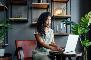 African American female freelancer making notes on laptop while sitting at table and working remotely at home