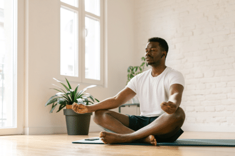 Young African American man sitting on yoga mat and meditating in yoga studio