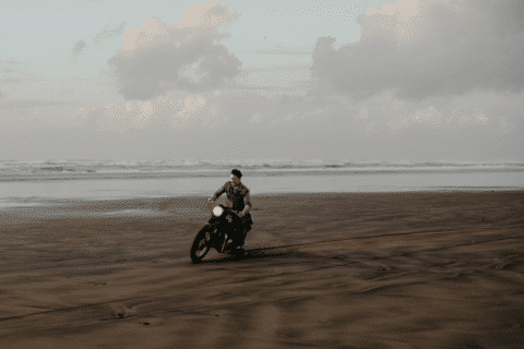Man riding a motorcycle on the sandy beach at sunset.
