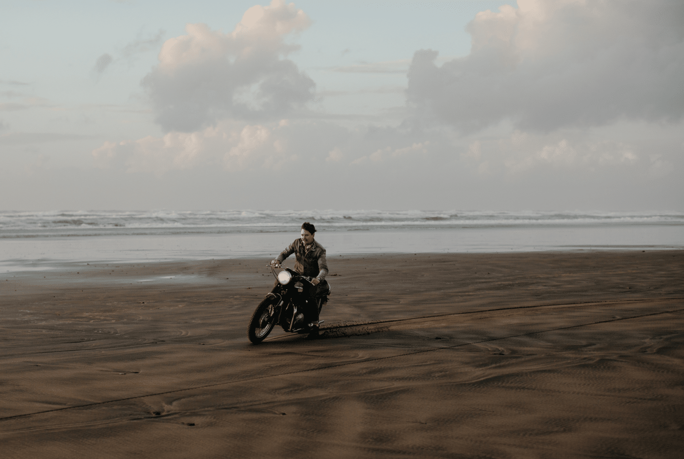 A man rides a motorcycle on a sandy beach at sunset.
