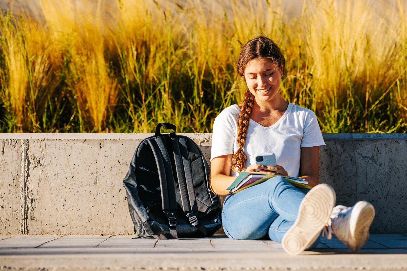 Portrait of a beautiful, young and intelligent-looking blonde braids college student woman wearing a white shirt and jeans smiling as she studies at the campus of her university