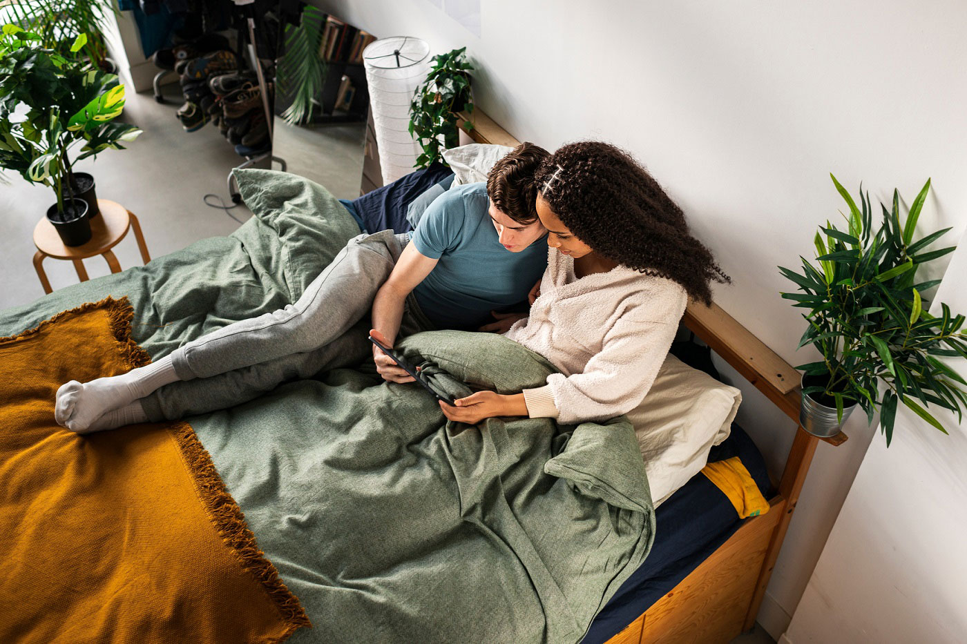 Candid multiracial couple browsing digital tablet snooping social media together in bed at their loft